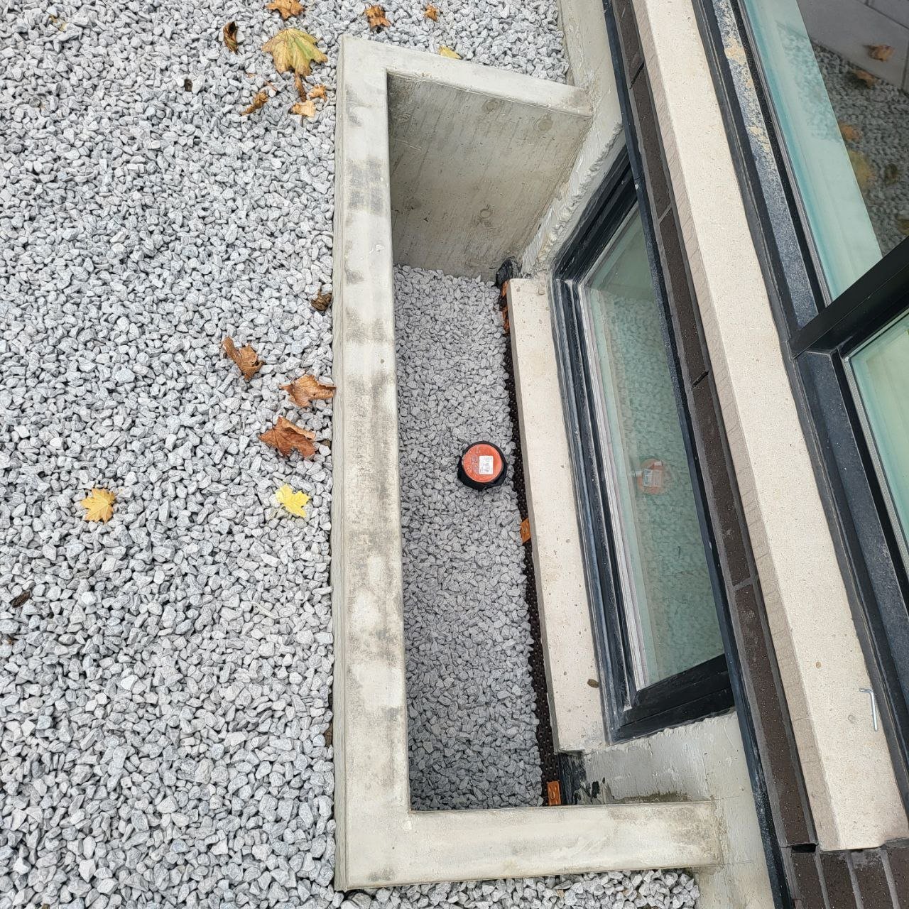 Top-down view of concrete window well with drainage gravel and weeping tile