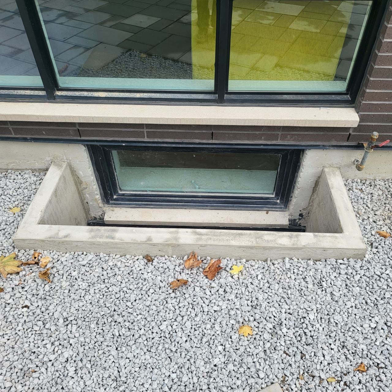 Wide view showing window well installation with gravel grading and landscaping