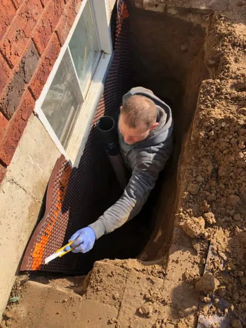 Toronto Waterproofing technician installing drainage membrane on a foundation